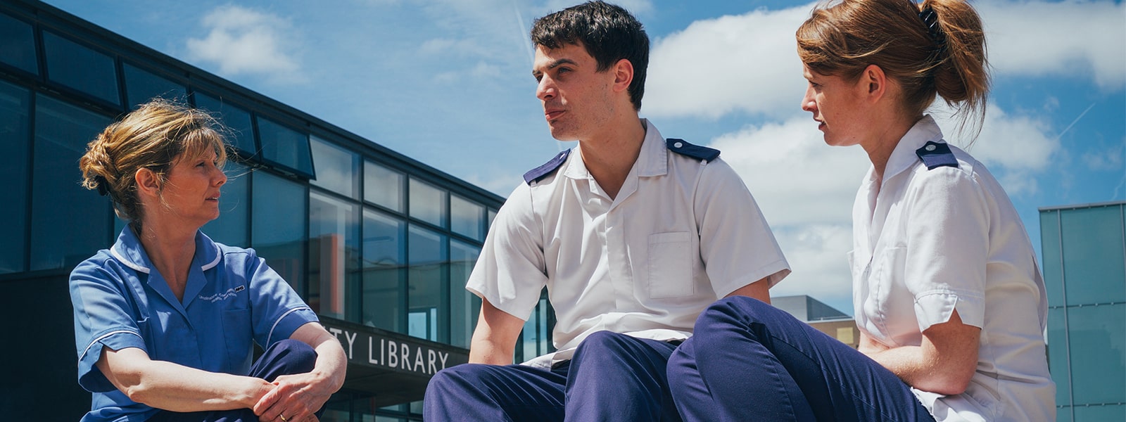 Three healthcare professionals sat outside the University of Lincoln Library in uniform