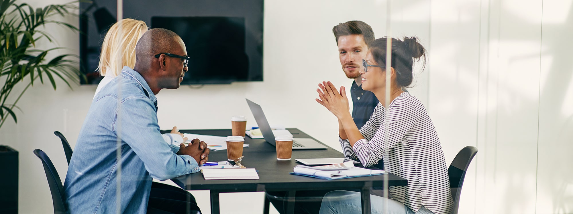 Four people sat behind a glass wall in a meeting room chatting