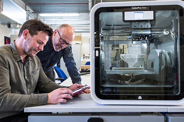 Two people looking at tablet with 3D printer on a table