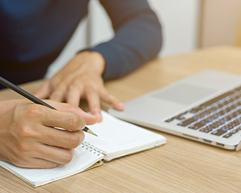 Person sat at desk with a laptop and writing pad