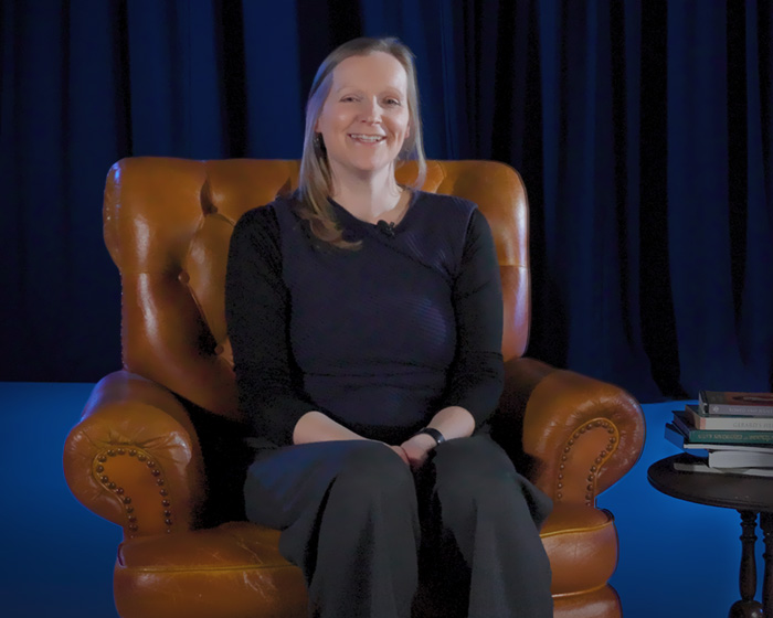 A woman sat in an armchair next to a table of books smiling