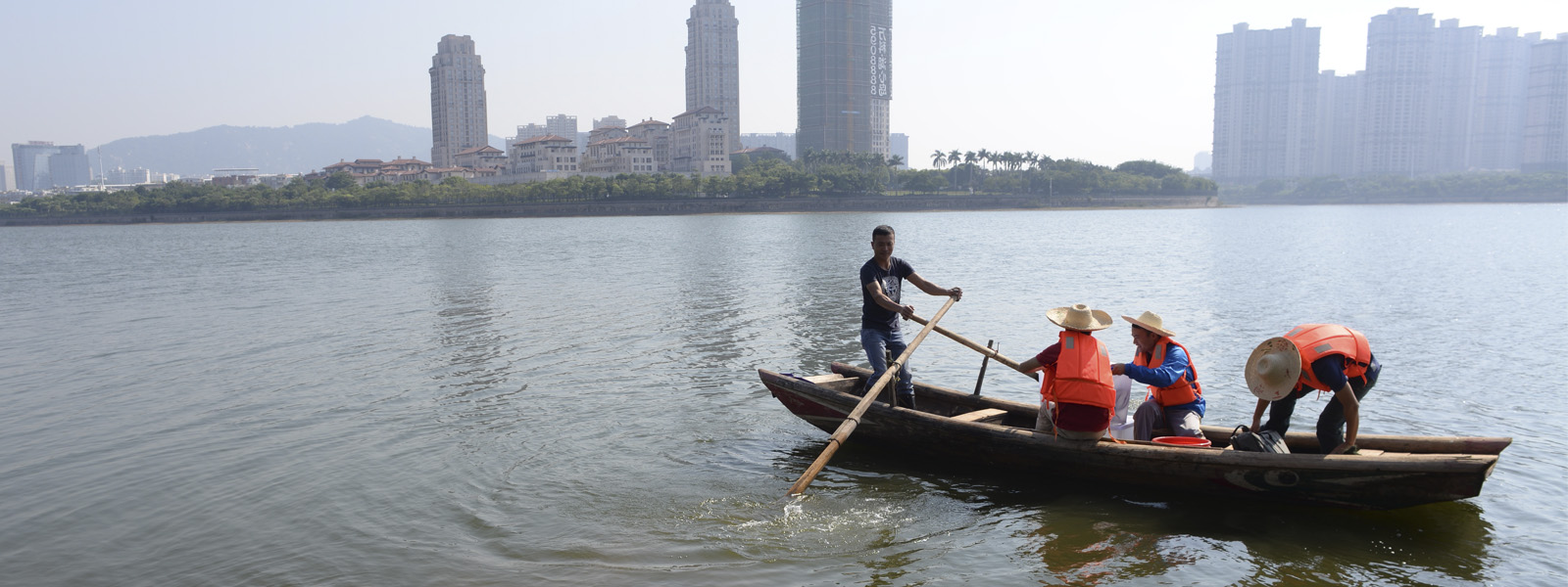 Men rowing a boat on a river with skyscrapers in the background