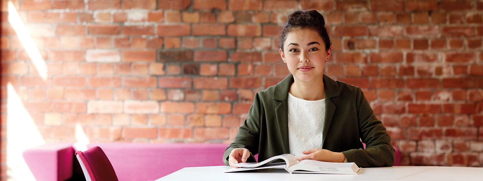 A student sat with a book and laptop