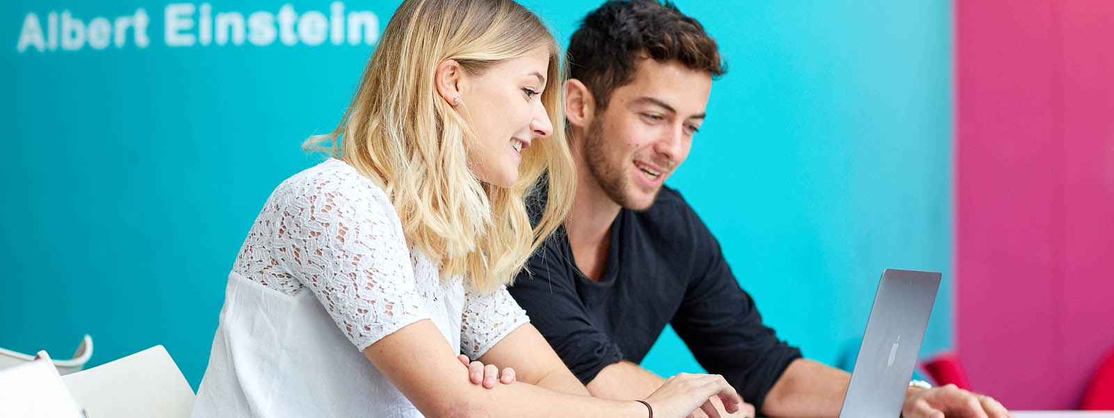 Two students working on a laptop in a study space